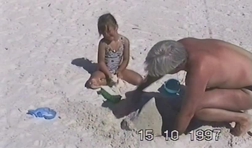 A father and young daughter build sandcastles together on a sunny beach in this charming vintage home video from 1997