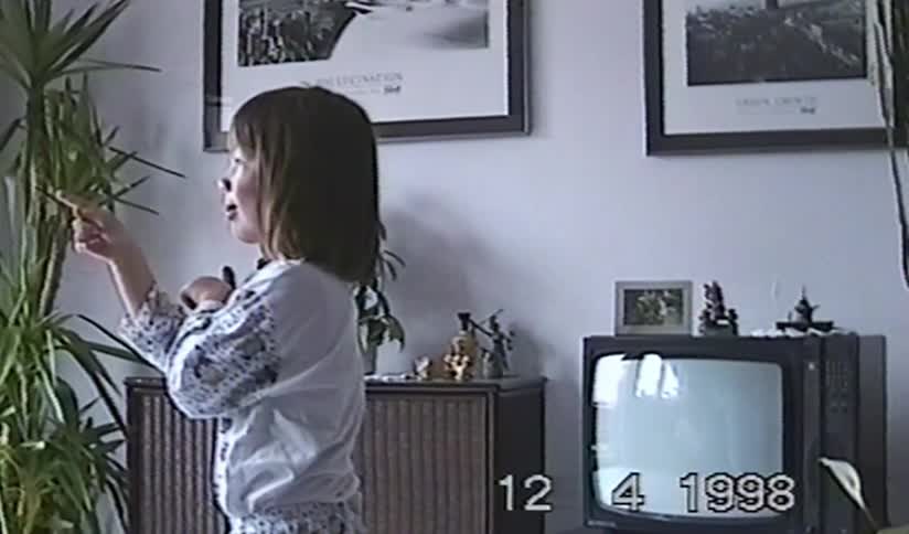 A young girl playfully poses and points around her living room in a vintage 1998 home video