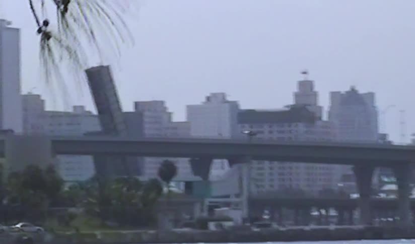 A vintage VHS panning shot captures the Miami, Florida skyline across the water on an overcast day in the 1990s