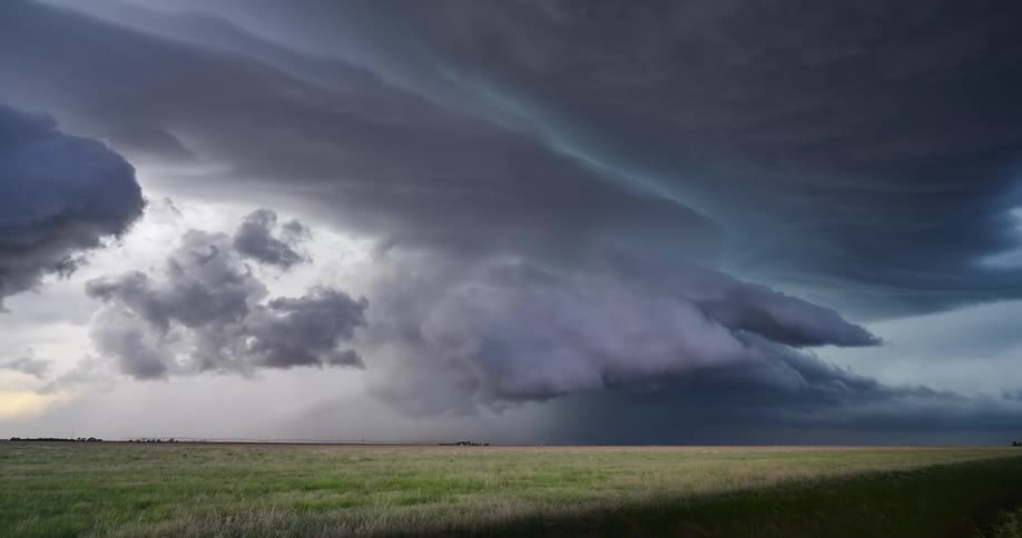 An ominous and awe-inspiring supercell thunderstorm with lightning flashes swirling above a wide-open grassy field