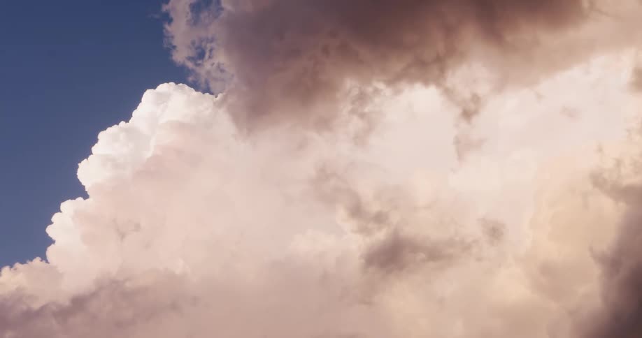 Majestic fluffy clouds with a pink hue slowly drift across a deep blue sky