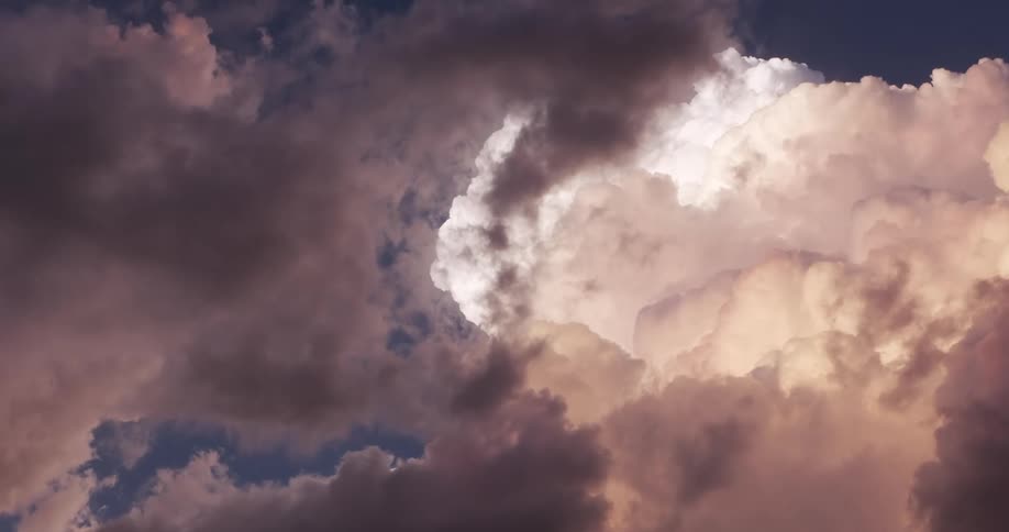 Majestic and dramatic storm clouds billow slowly across a deep blue sky, illuminated by the setting sun