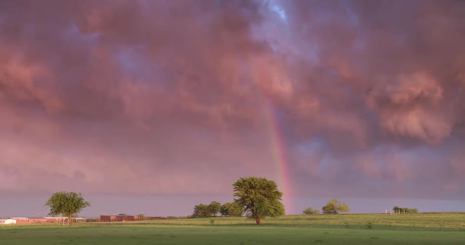 A stunning double rainbow arcs across a sky filled with dramatic pink storm clouds over a tranquil green countryside