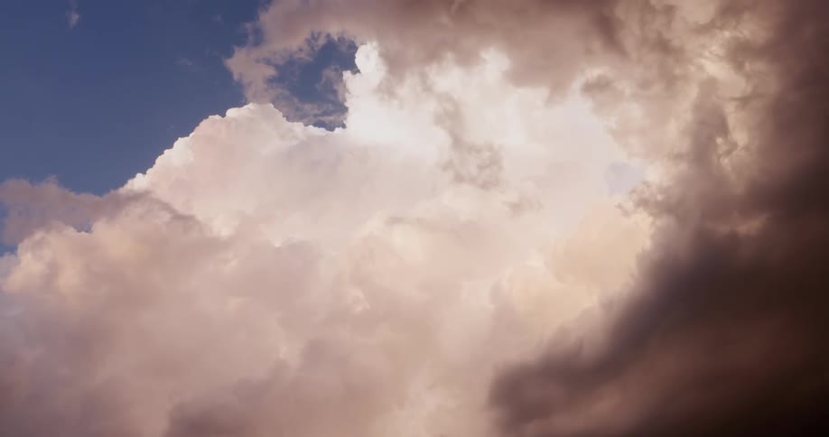 A serene view of billowing cumulus clouds, with dark storm fronts and sunlit peaks against a blue sky