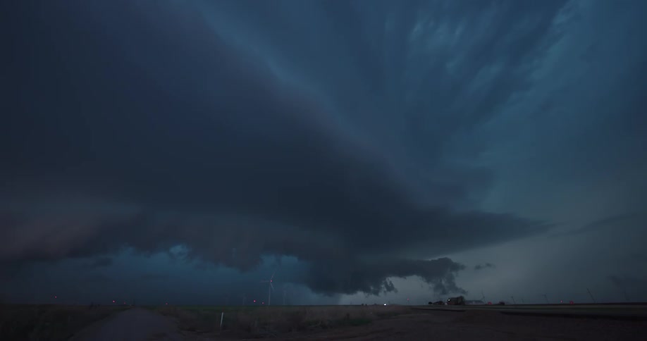 A powerful supercell thunderstorm unleashes dramatic lightning strikes over a rural wind farm at night