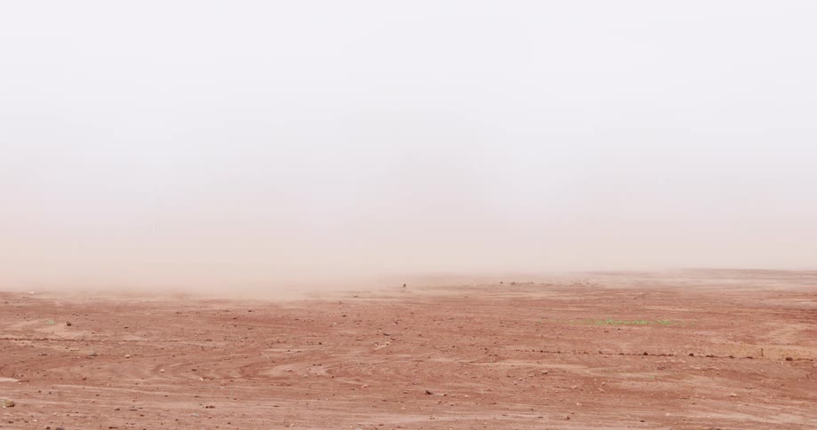 A strong wind blows dust and sand across a vast, arid landscape during a powerful dust storm