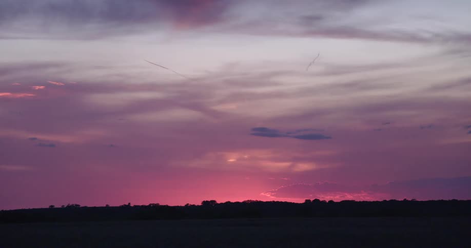 A vibrant pink and purple sunset glows on the horizon over a silhouetted landscape
