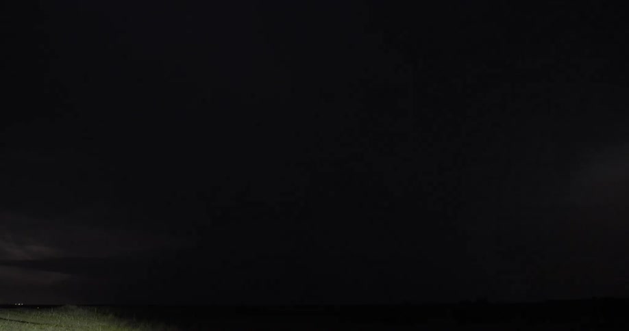Massive lightning bolts strike down from the night sky over a rural field with cows during a dramatic thunderstorm