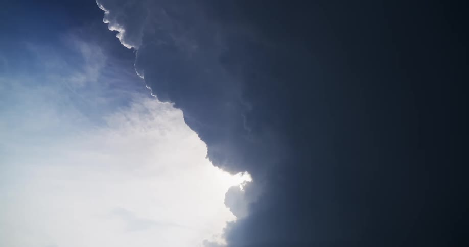 A dramatic vertical view of the sky contrasts a bright sunlit area with a massive, dark, and ominous storm cloud