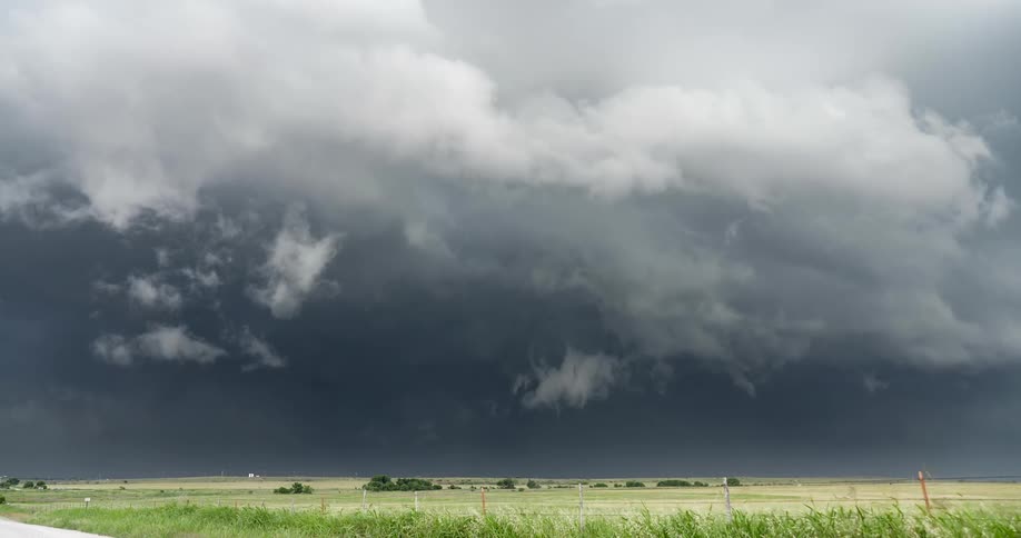 Ominous and dramatic supercell storm clouds gather and move over a vast rural landscape