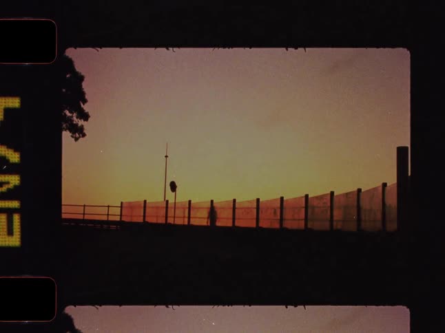 Nostalgic old film captures the Toronto skyline at sunset from a highway overpass, featuring a silhouetted figure walking against the golden hour sky