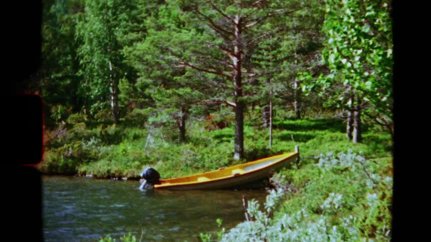 Archival 8mm footage captures a peaceful scene of a yellow boat docked on a serene river amidst a verdant summer forest