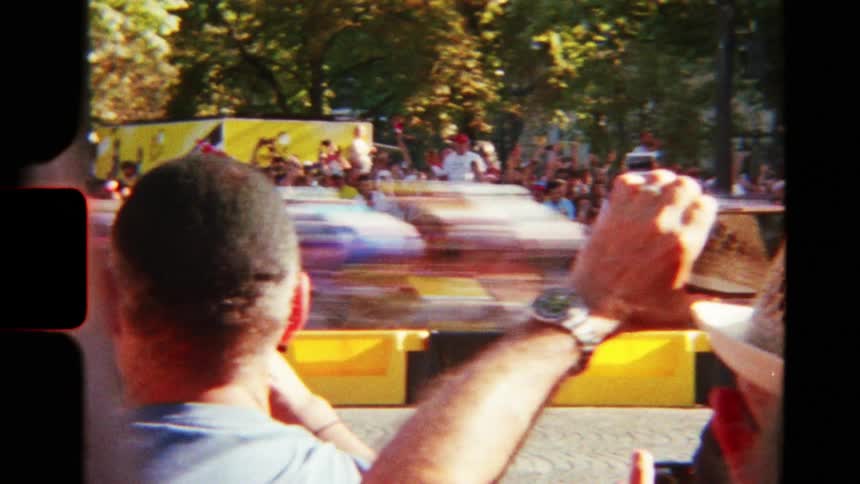Vintage 8mm film captures the blurred motion of the Tour de France peloton as they speed past a crowd of cheering spectators in Paris