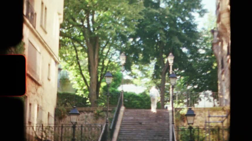 A vintage Super 8mm film follows a person walking up a long, tree-lined staircase in a charming European city