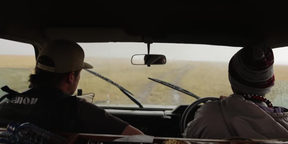 Men driving through a field as it rains