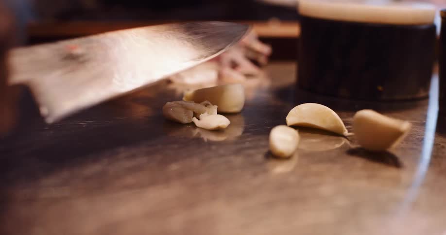 Close-up slow-motion shot of a chef's hands meticulously chopping fresh garlic cloves on a stainless steel kitchen counter