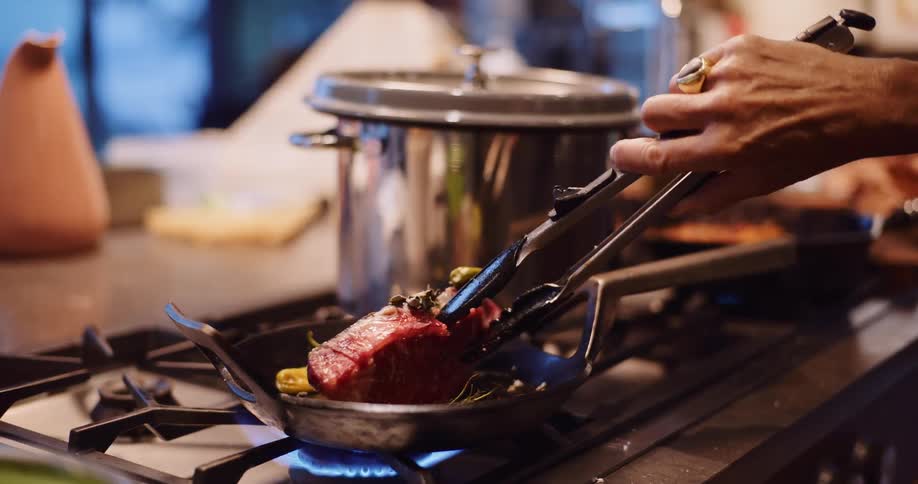 A chef carefully sears a thick-cut steak in a hot skillet on a gas stovetop, filmed in beautiful slow motion