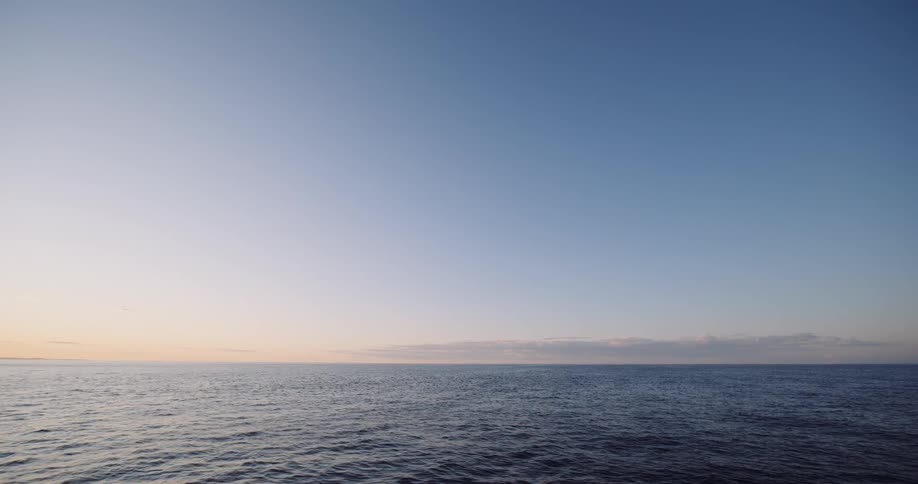 A serene view of the calm open ocean meeting a clear blue sky at the horizon