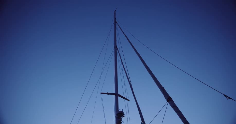 A sailboat mast is silhouetted against the deep blue sky during the quiet twilight hour