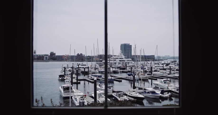 A serene view through a window of a bustling marina filled with boats and yachts docked on a calm day