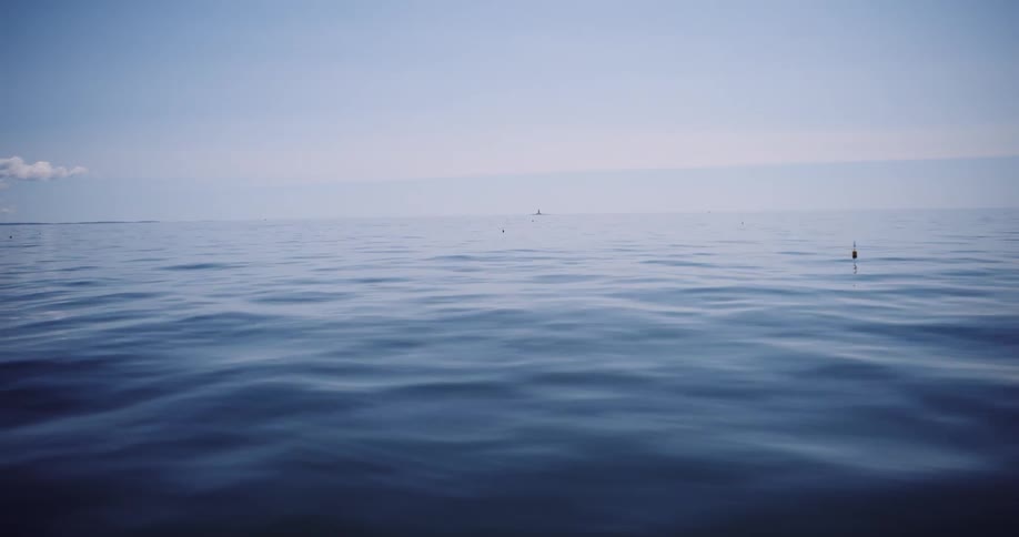 A lone fishing float bobs on the calm, deep blue surface of the open ocean under a hazy sky