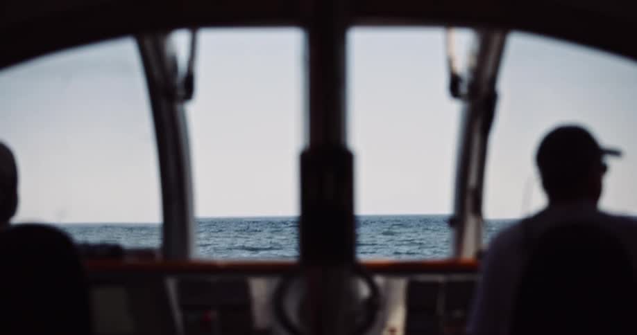 A peaceful view from the inside of a boat's cabin shows a silhouetted captain looking out over the calm ocean