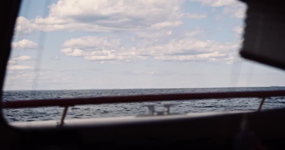 The open sea ripples under a cloudy sky as seen from the interior of a moving boat