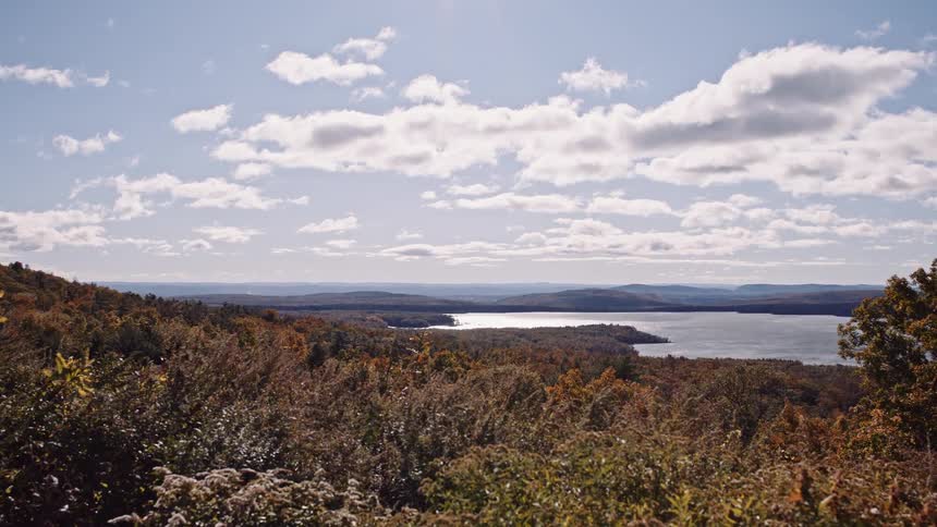A stunning wide shot from a high vantage point overlooking a vast lake and colorful autumn forest on a sunny day