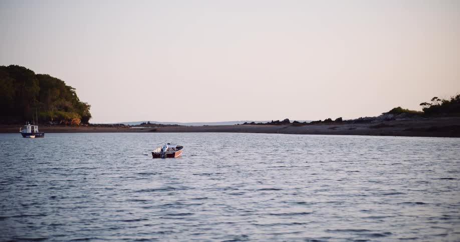 A small motorboat bobs gently in a quiet bay as the sun begins to set over the calm water