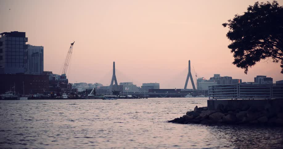 A serene view of the Leonard P. Zakim Bunker Hill Memorial Bridge and the Boston skyline across the water at sunset