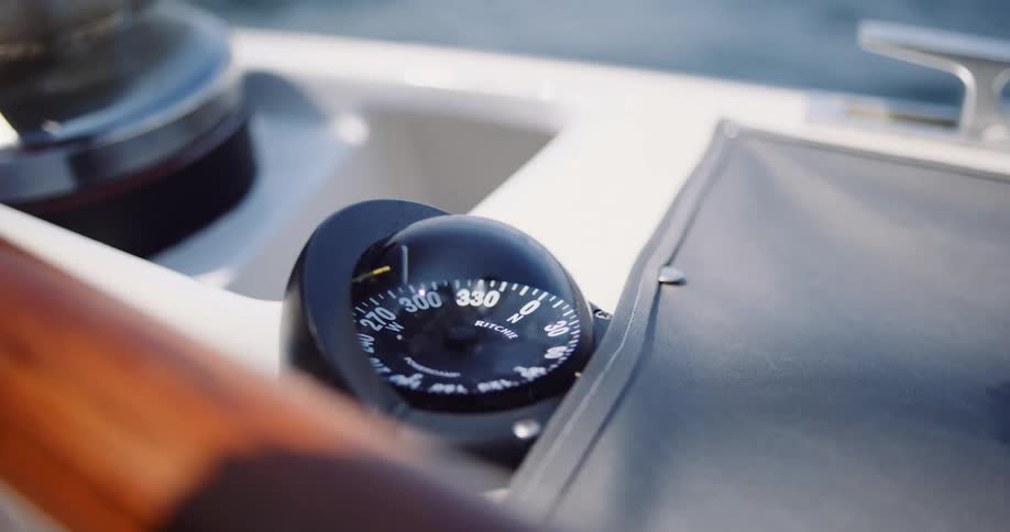 A close-up of a sailboat's compass as it rocks back and forth while navigating through the ocean water on a sunny day