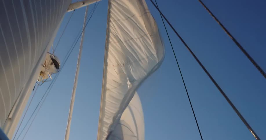 A slow pan upwards reveals the full sails of a sailboat against a clear blue sky