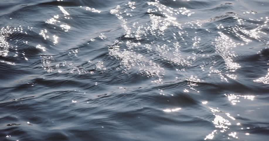 Slow motion close-up of dark blue ocean water as gentle ripples catch the sunlight and create sparkling reflections