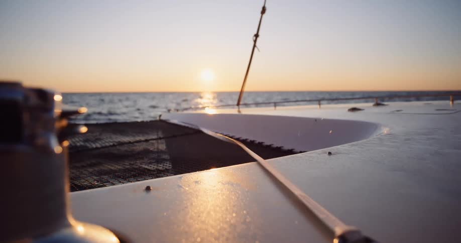 A tranquil close-up shot from the deck of a catamaran sailing peacefully across the ocean during a beautiful golden sunset
