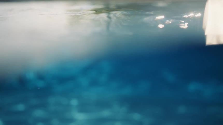 A serene split-shot perspective slowly submerges into the deep blue water, capturing the gentle ripples and dreamy light refractions