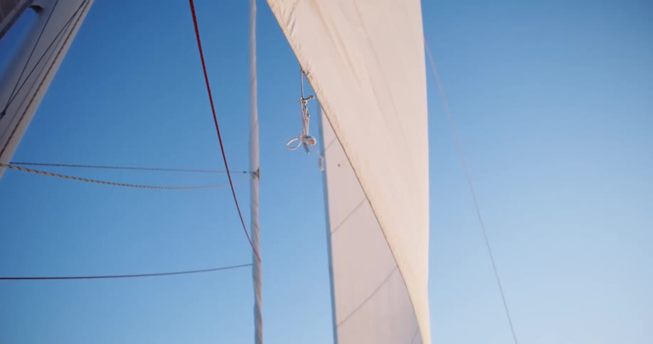Low-angle shot of a white sailboat sail flapping gently in the wind against a clear blue sky