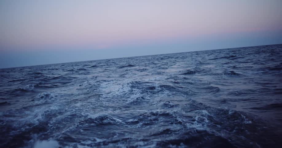 A serene slow-motion view of the wake behind a boat on the vast open ocean during a calm twilight
