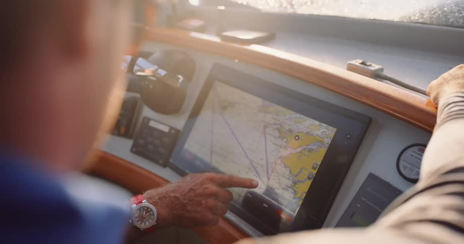 Two men at the helm of a boat use a touchscreen GPS to plan their course at sea with a sunny lens flare
