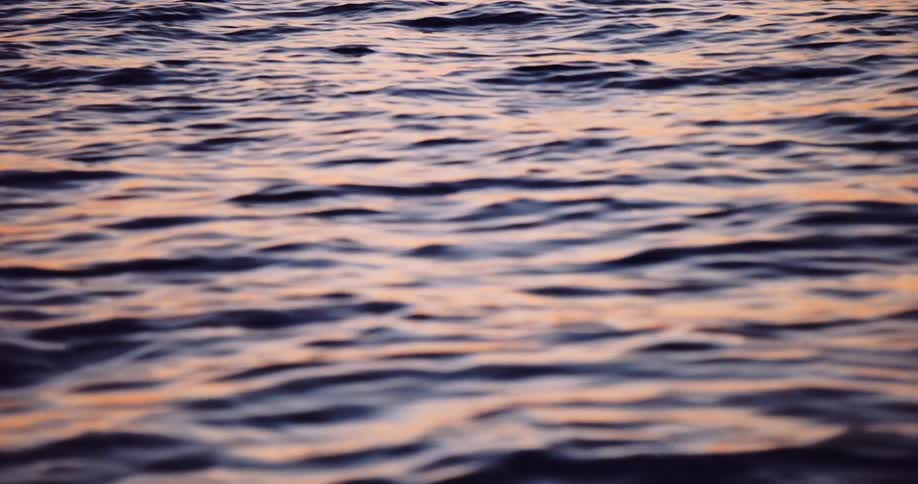Calm ocean water ripples gently, reflecting the warm colors of a peaceful sunset