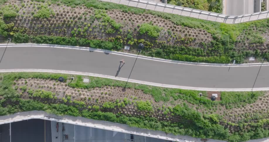 Top-down descent over a woman running on a modern green pedestrian bridge over a multi-lane highway