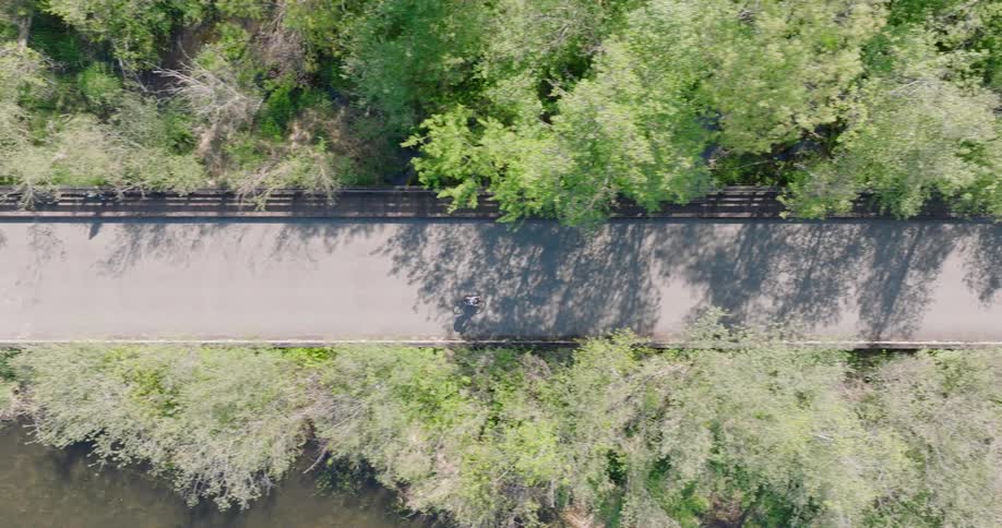 Birds eye view of a cyclist riding on a trail with dappled morning light streaming through the trees