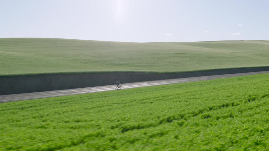 A cyclist enjoys a serene ride along a quiet country road surrounded by rolling green hills on a sunny day