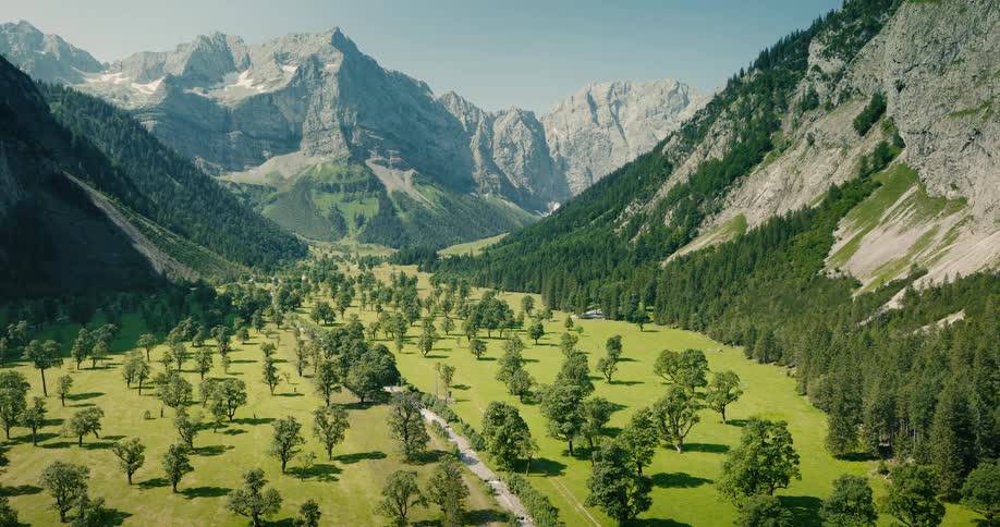 A breathtaking aerial view slowly reveals a vibrant green valley floor dotted with trees, nestled between majestic, towering mountain peaks