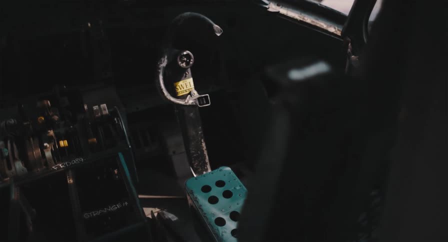 A moody, static shot of a forgotten airplane's control column and rudder pedal inside a dark, derelict cockpit