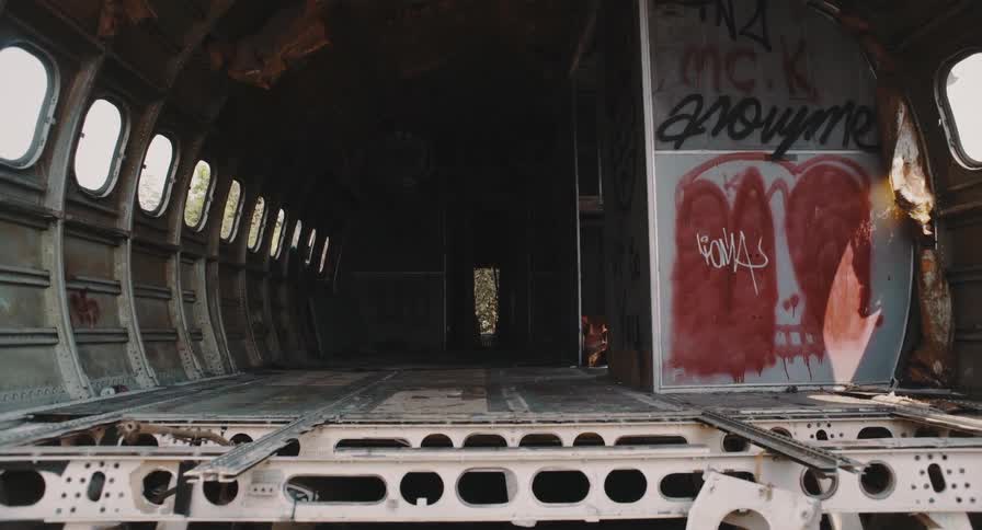 A slow push-in shot of the dark and eerie interior of a stripped, abandoned airplane fuselage covered in graffiti