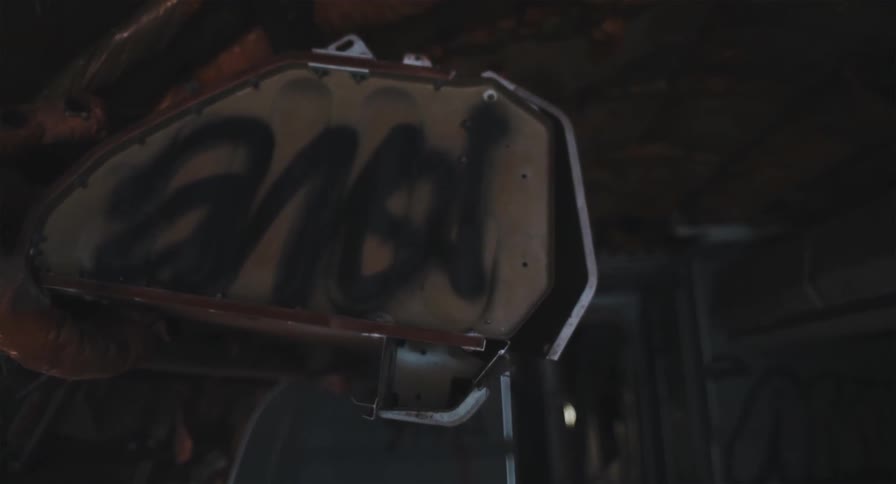 A static close-up shot of graffiti spray-painted on a rusted metal object inside a dark, abandoned vehicle