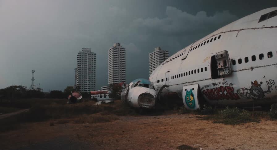 A post-apocalyptic scene shows a graffiti-covered wrecked plane in a field against a backdrop of city skyscrapers and a stormy sky