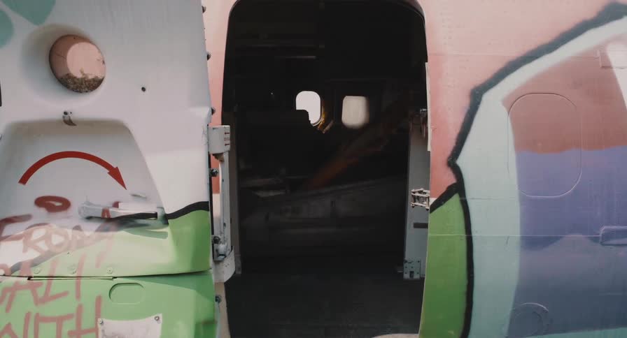 A view into the dark and abandoned interior of a graffiti-covered airplane through an open doorway