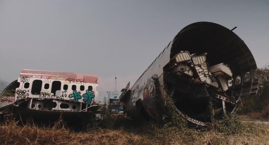 A time-lapse of an abandoned and graffiti-covered airplane wreckage in a field with clouds passing overhead