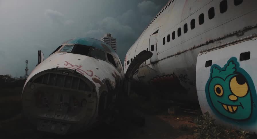 A spooky cinemagraph shows derelict airplanes with graffiti decaying in an aircraft graveyard under dark, moving clouds